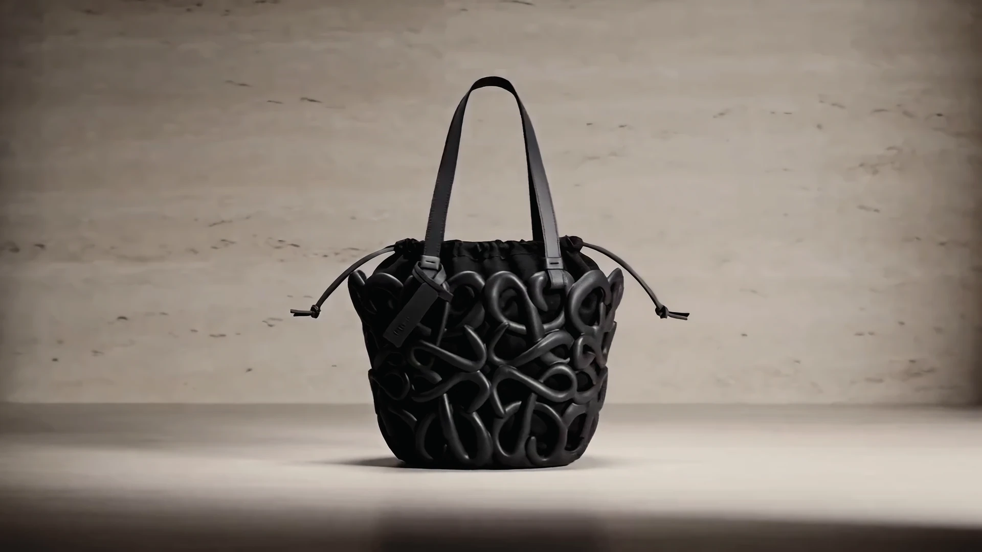 The finished bag on a travertine plinth: a black lattice cage around a soft black drawstring pouch.